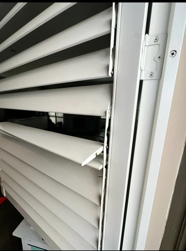 White plantation shutter louvres partly open, looking into a living room