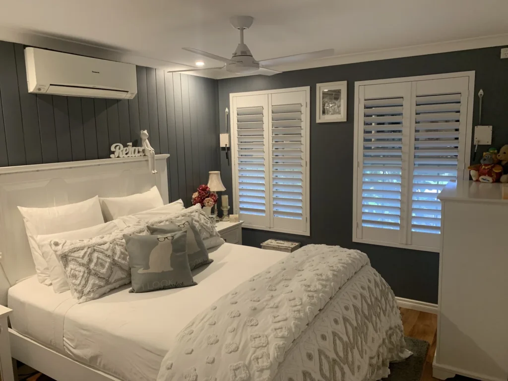 Two sets of white plantation shutters in a bedroom with navy panelled walls