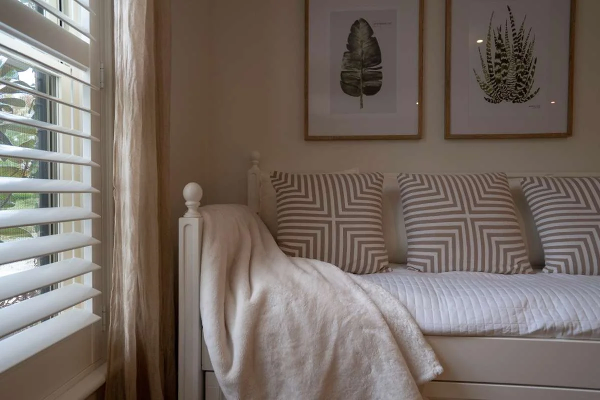 Bedroom with a made bed, cushions and artwork beside plantation shutters