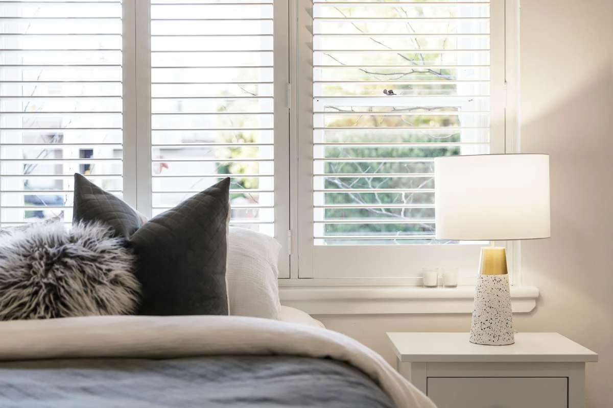 Bedroom with a bedside lamp, cushions and white plantation shutters
