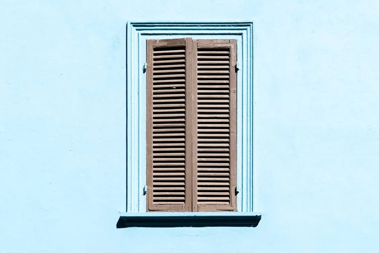Grey shutters on a window against a blue wall