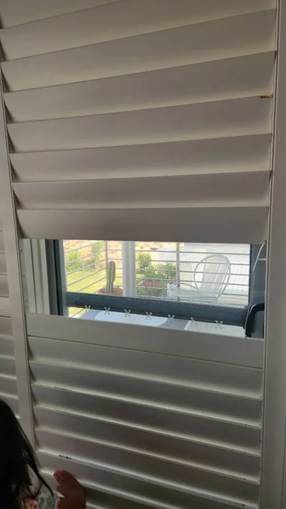 Repaired white plantation shutters with a view out to a balcony