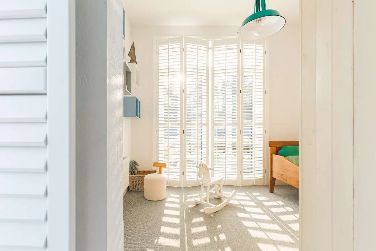 Sunlit nursery with a rocking horse and full-height plantation shutters